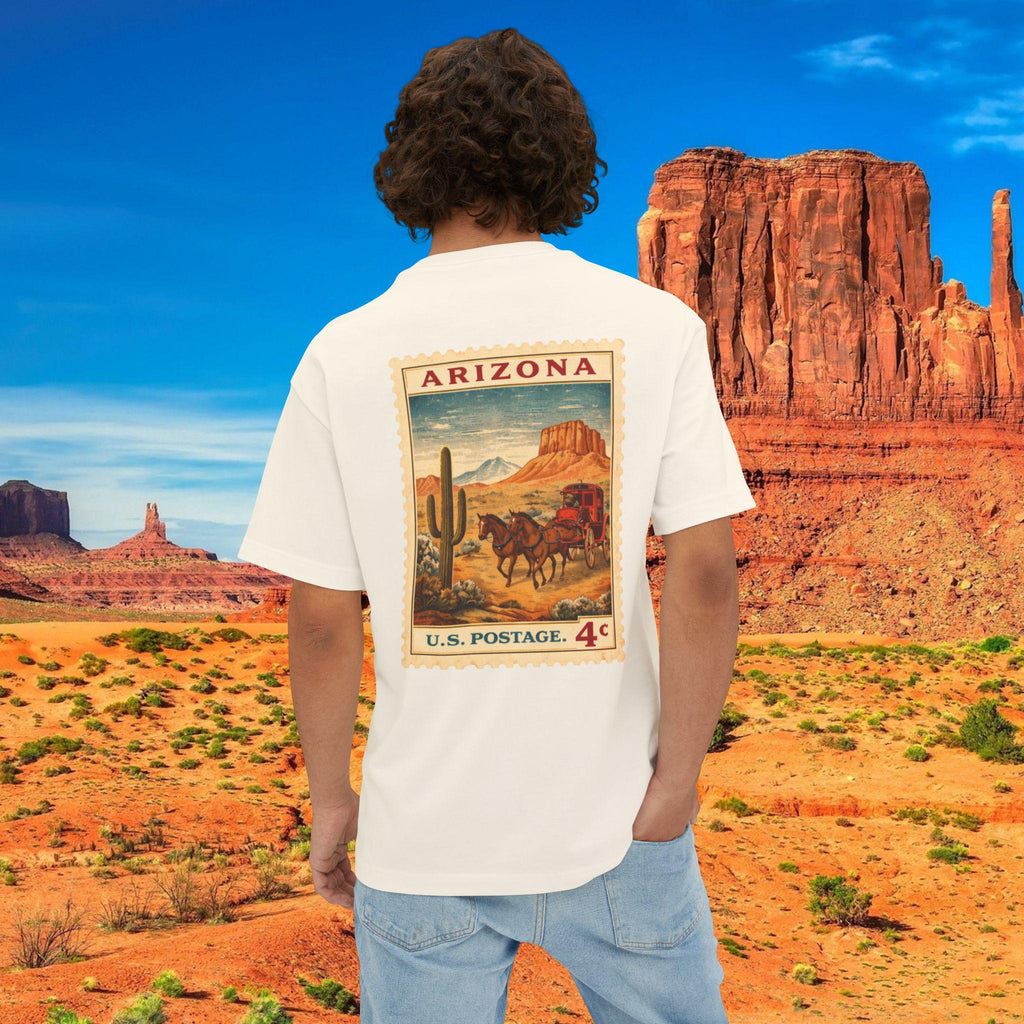 May include: Cream-colored t-shirt featuring a vintage Arizona postage stamp design on the back. The stamp depicts a desert landscape with a horse-drawn carriage, cactus, and the text "Arizona" and "U.S. Postage. 4¢".