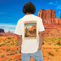 May include: Cream-colored t-shirt featuring a vintage Arizona postage stamp design on the back. The stamp depicts a desert landscape with a horse-drawn carriage, cactus, and the text "Arizona" and "U.S. Postage. 4¢".
